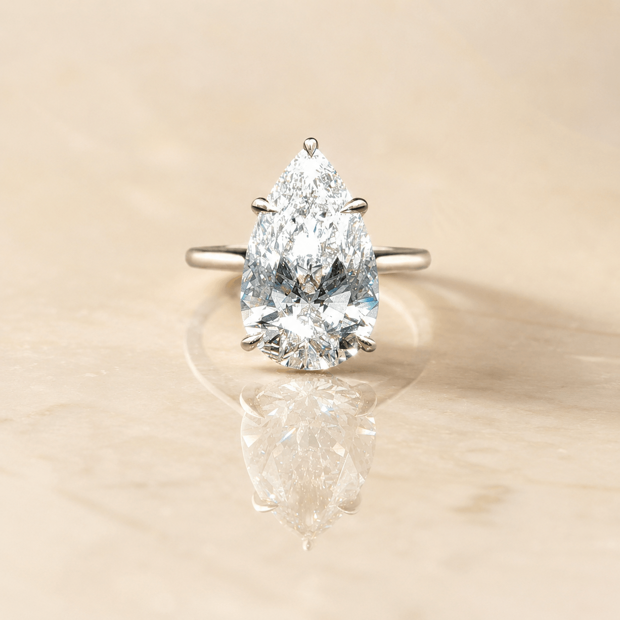 Finished pear-shaped diamond engagement ring on a warm ivory reflective surface